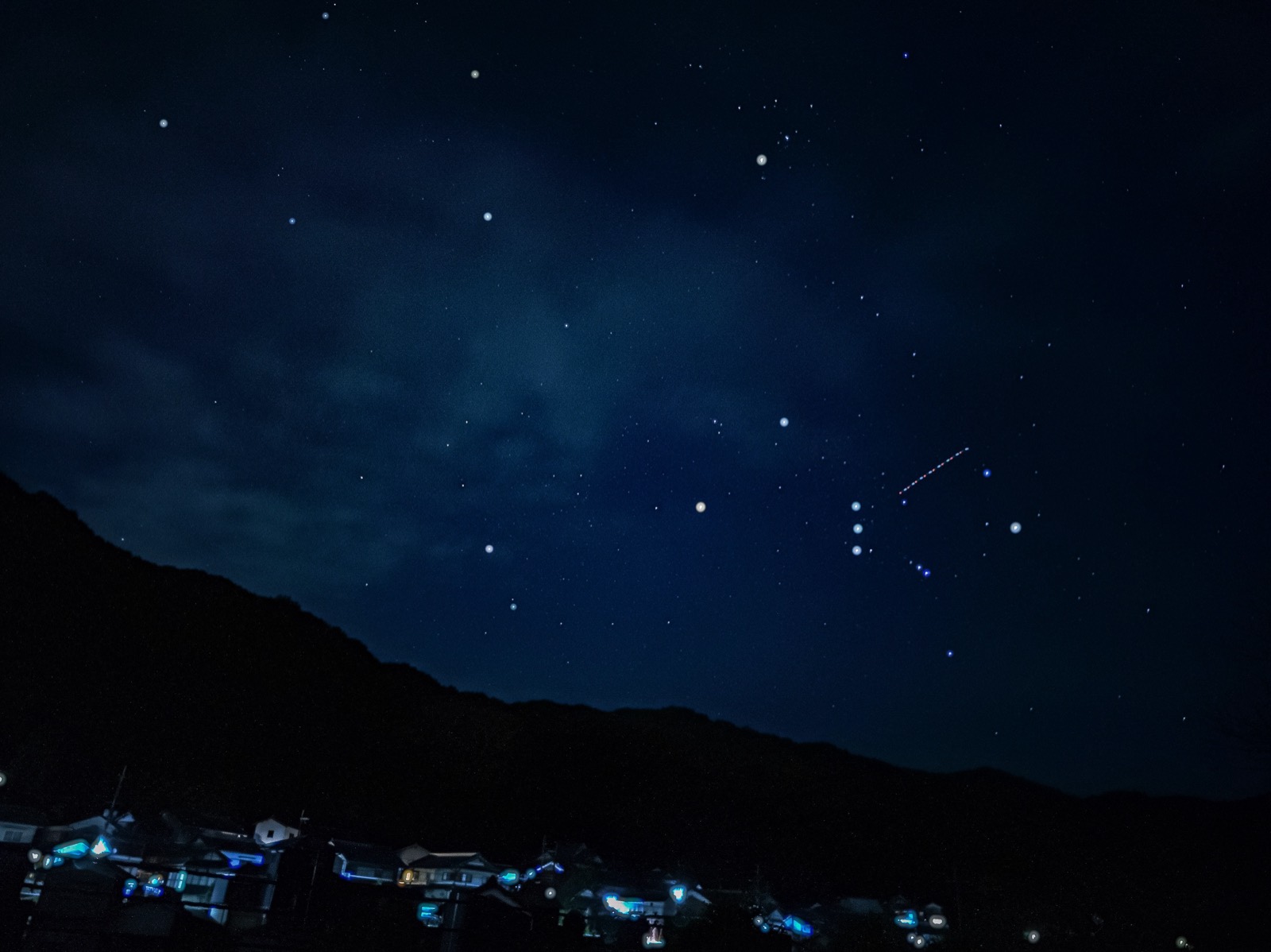 濃紺の夜空に星が散り、山のふもとに集落の灯りが並ぶ