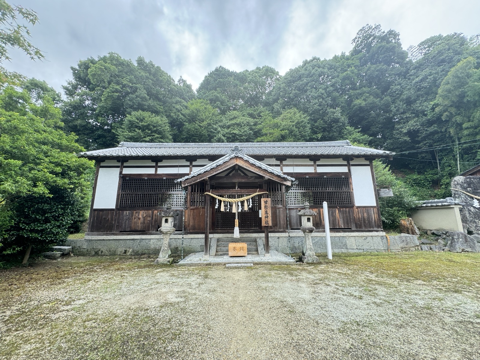 木立を背にした甘樫坐神社の社殿。前に一対の石灯籠が立つ