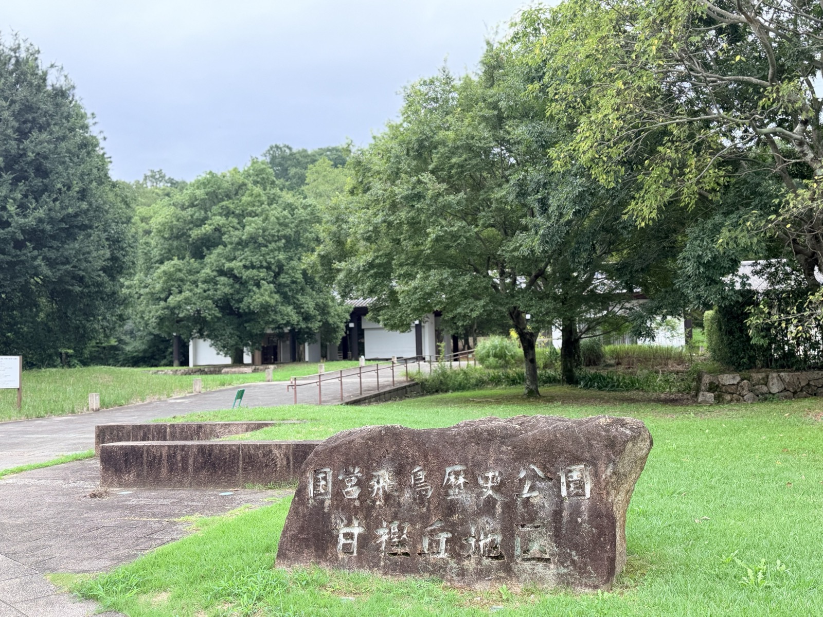 「国営飛鳥歴史公園 甘樫丘地区」と刻まれた石碑。奥に木立と休憩所の建物