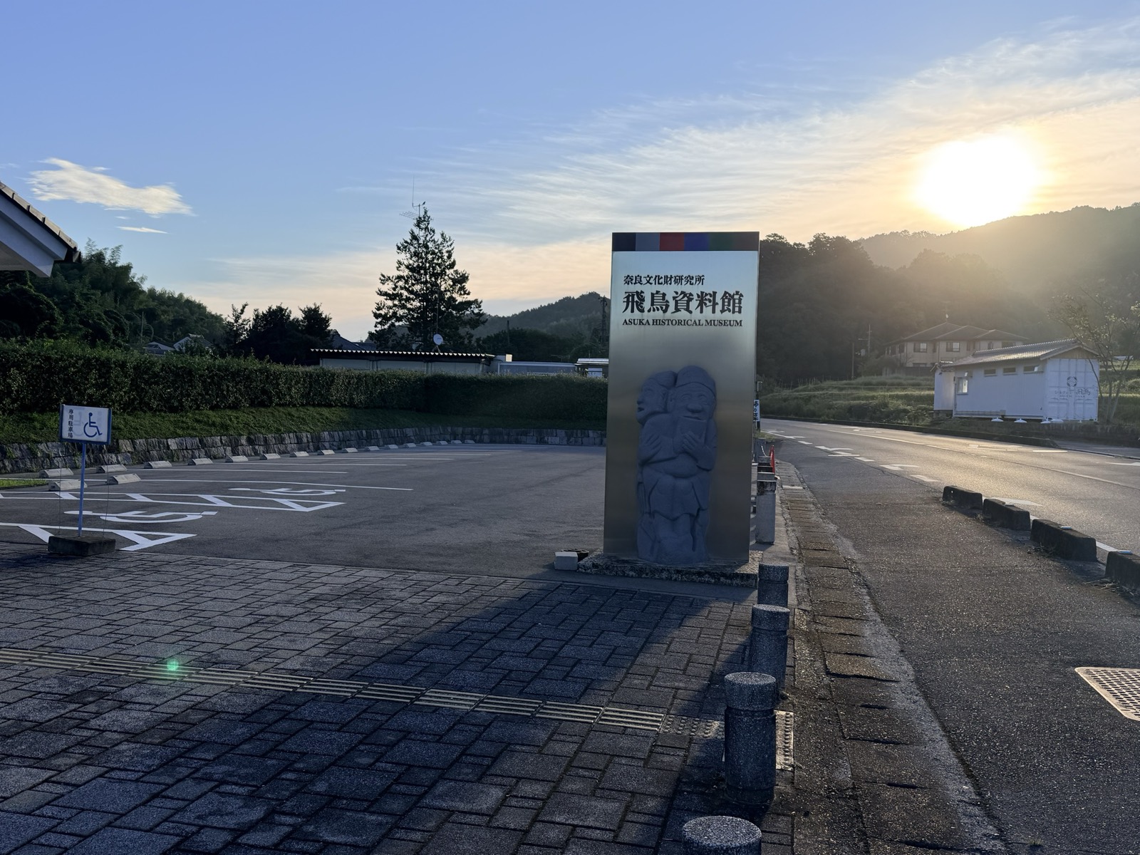 The museum sign in the car park, carved with a relief of a stone figure, as the morning sun rises over the hills behind