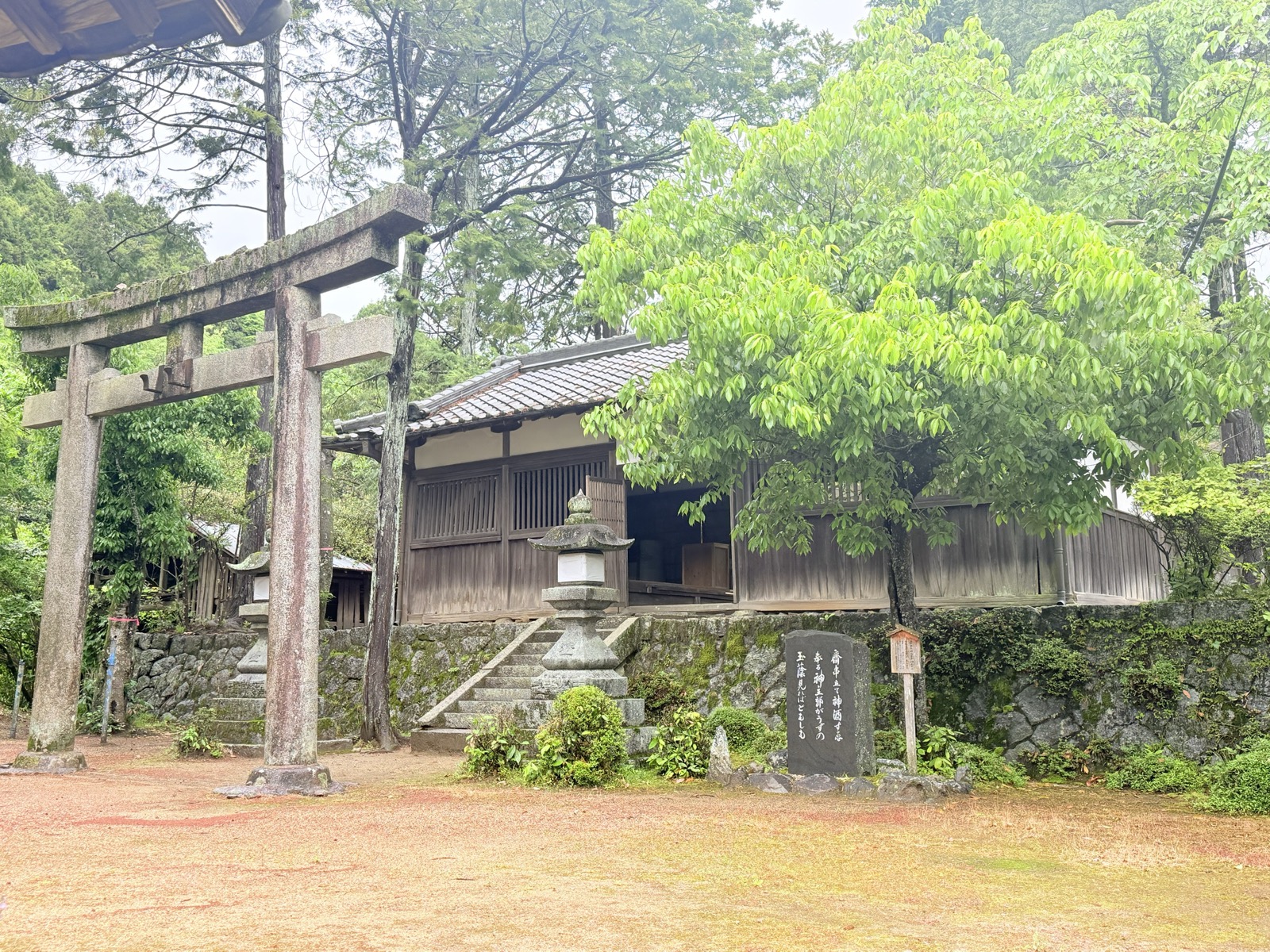 石鳥居の奥に横たわる加夜奈留美命神社の拝殿。手前に灯籠と歌碑