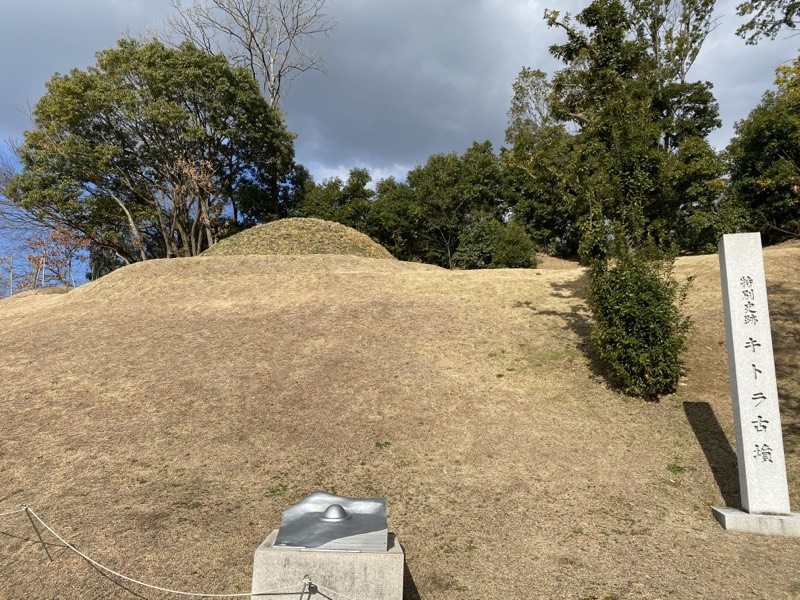 芝に覆われたキトラ古墳の墳丘と、「特別史跡 キトラ古墳」の石標