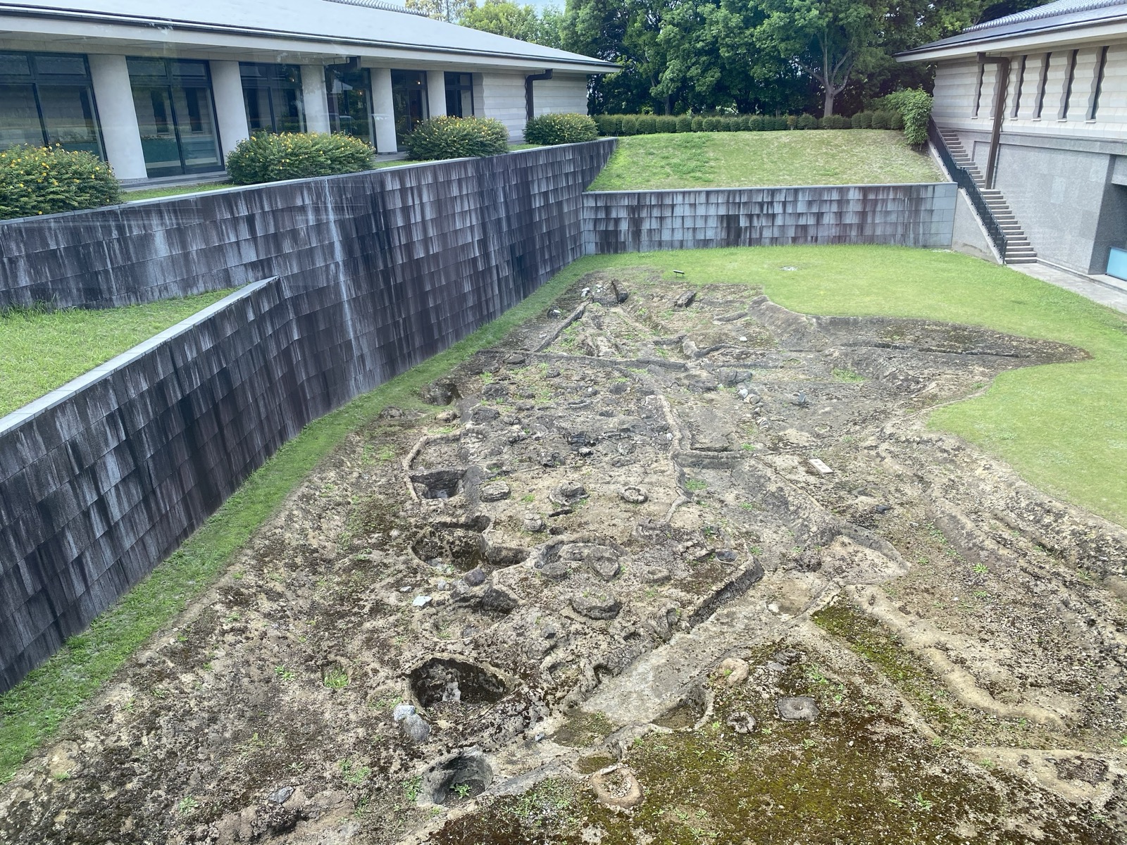 建物のあいだに露出展示された飛鳥池工房遺跡の遺構。石組みや炉の跡が地面に並ぶ