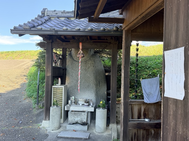 瓦屋根のお堂に納められた弥勒石。鈴緒が下がり、手前に花と供え物が置かれている