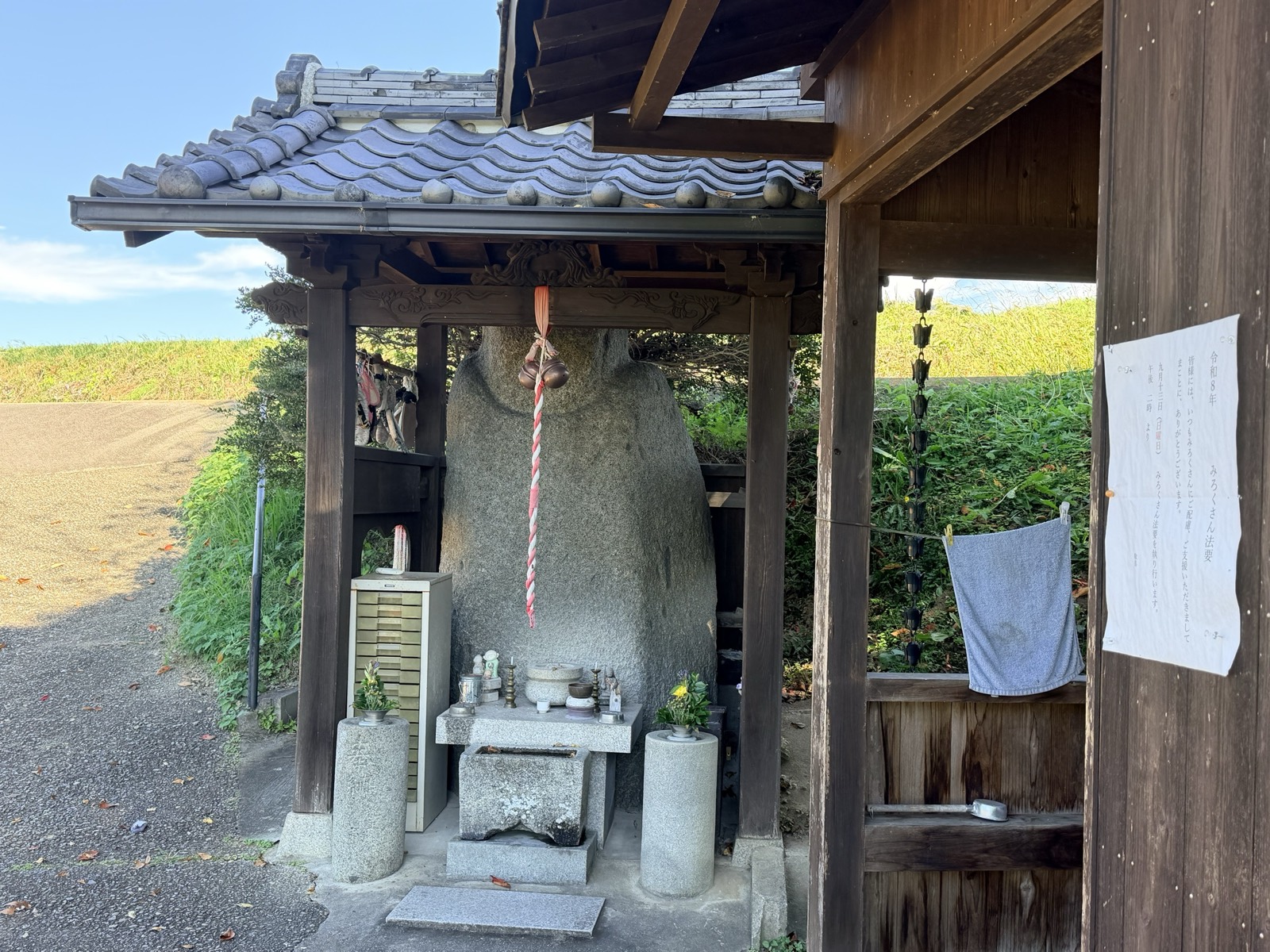 瓦屋根のお堂に納められた弥勒石。鈴緒が下がり、手前に花と供え物が置かれている