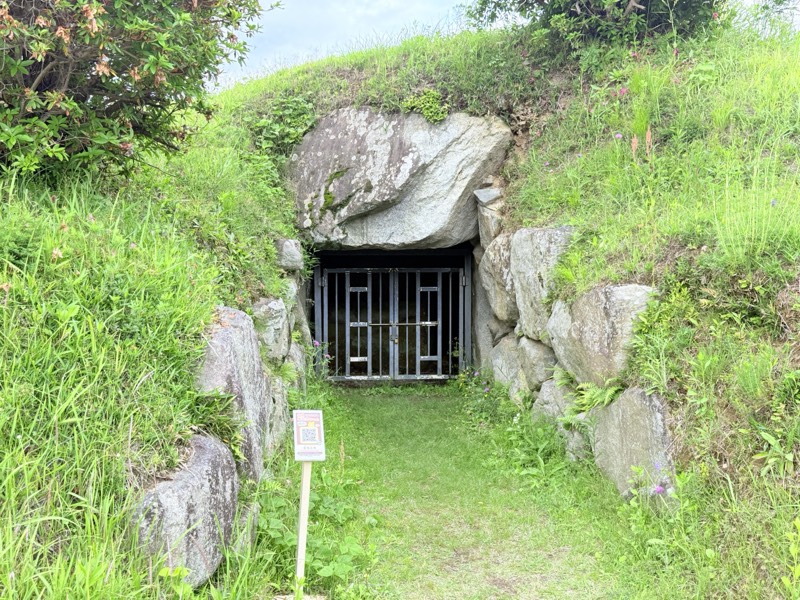 草に覆われた都塚古墳の墳丘と、柵の付いた横穴式石室の入口