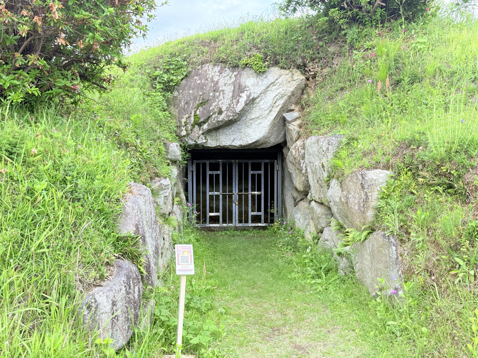 草に覆われた都塚古墳の墳丘と、柵の付いた横穴式石室の入口