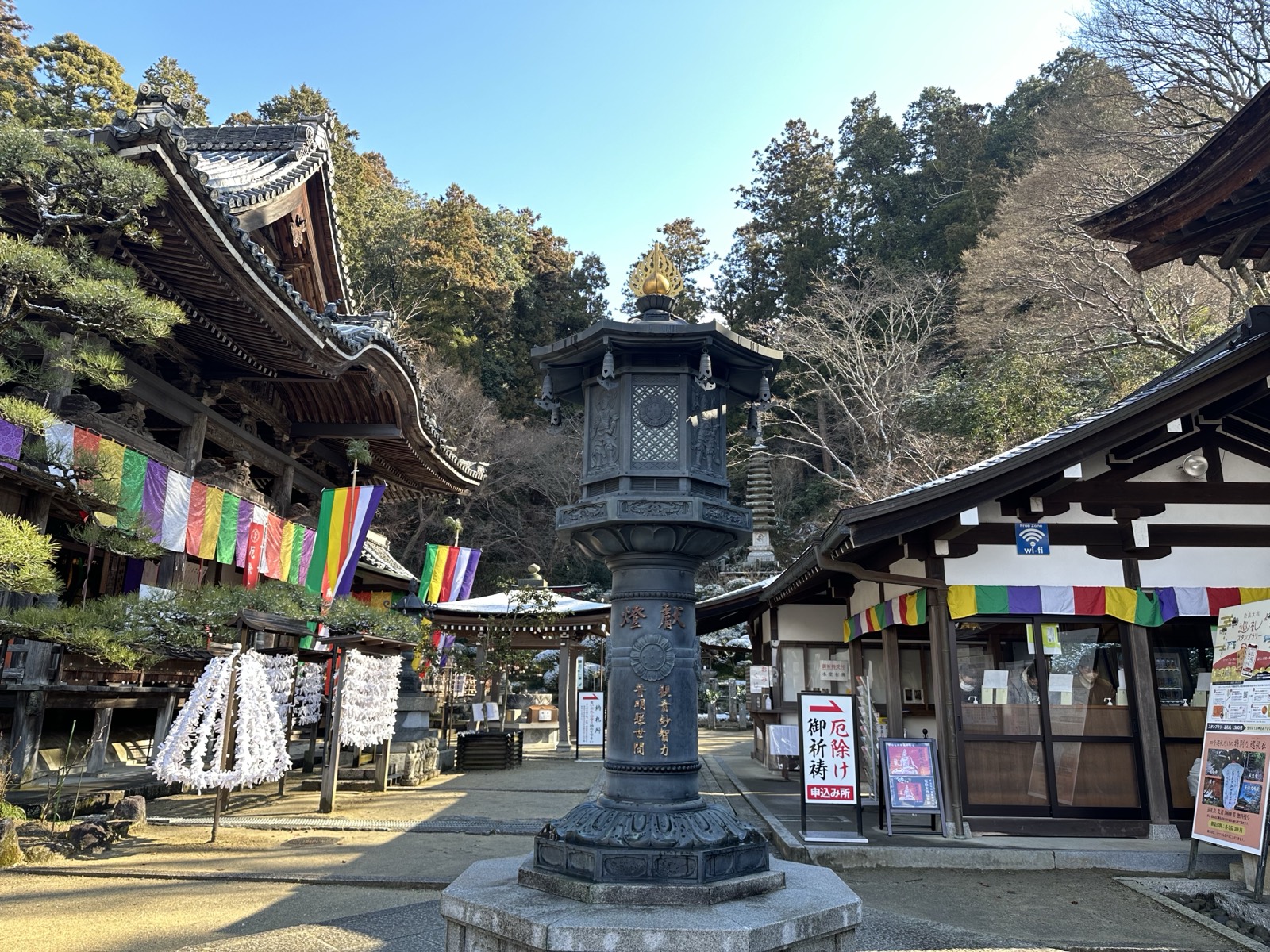冬の岡寺境内。五色幕と厄除けの幟がかかり、中央に献燈の灯籠が立つ
