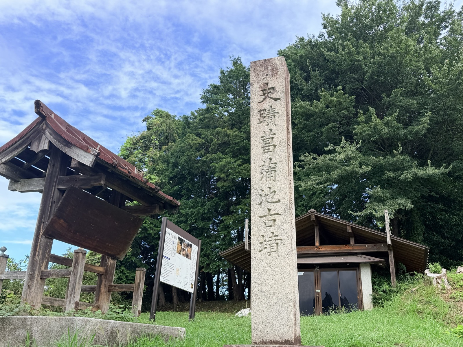 「史蹟 菖蒲池古墳」と刻まれた石碑。奥に覆屋と説明板